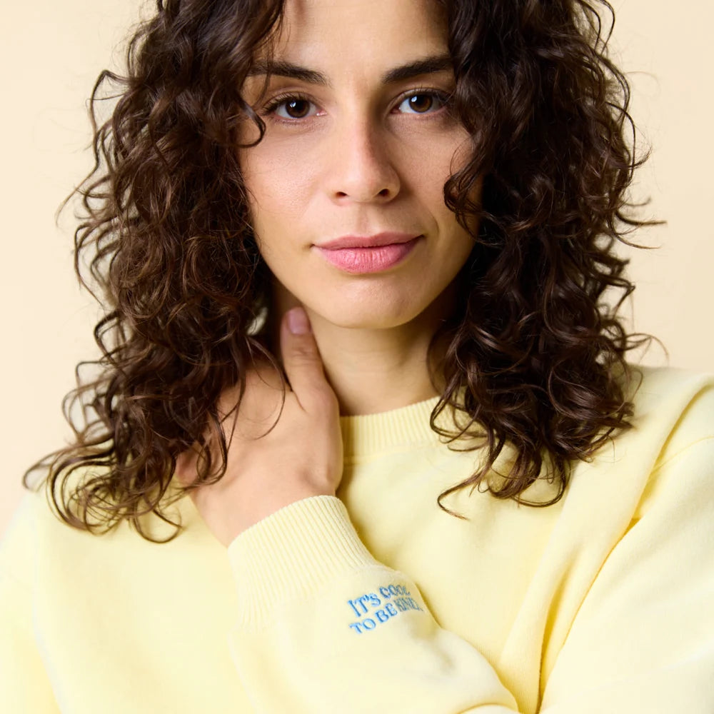 Nahaufnahme des buttergelben Sweaters mit blauer Stickerei am Ärmel.