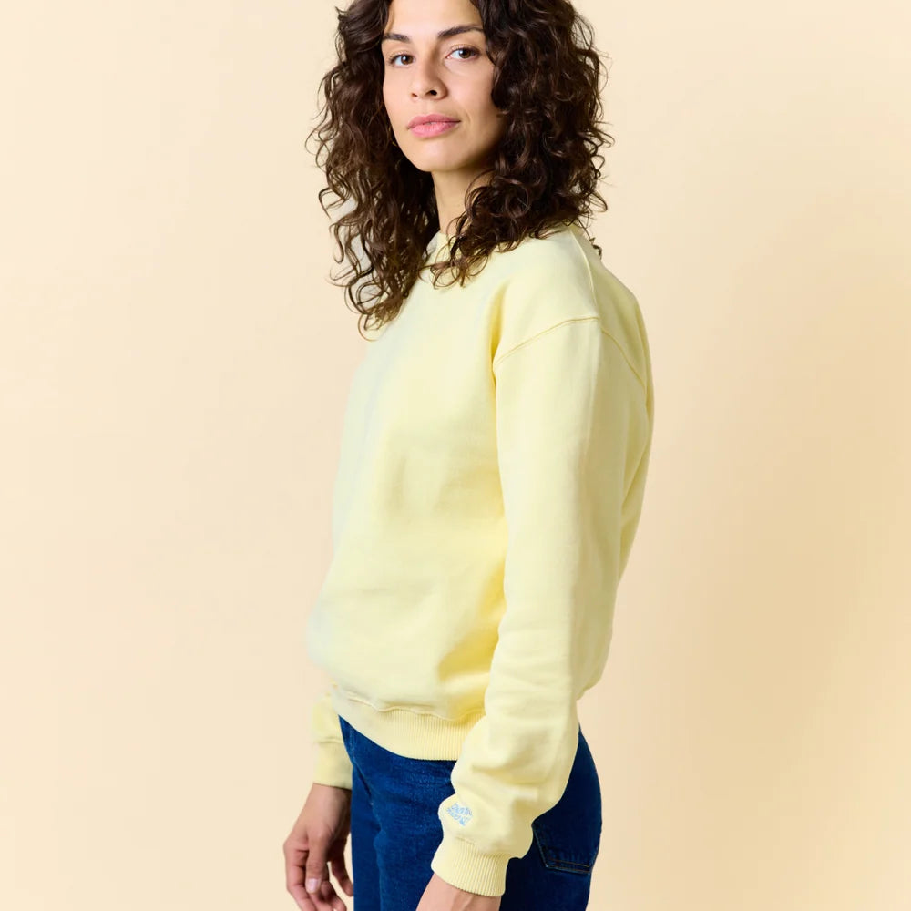 Seitenansicht des buttergelben popeia Sweaters, kombiniert mit einer Jeans.