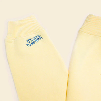 Blaue Stickerei „It’s cool to be kind“ am Ärmel des buttergelben Sweaters.