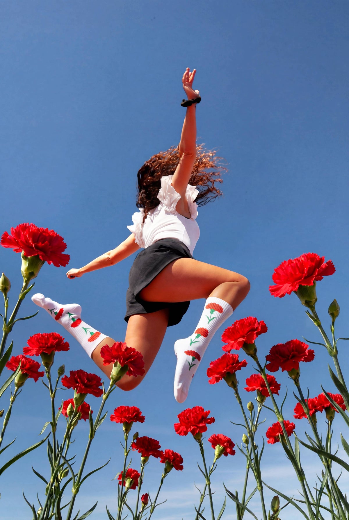 Person mit weißen Freedom Socken springt über ein Feld aus roten Nelken